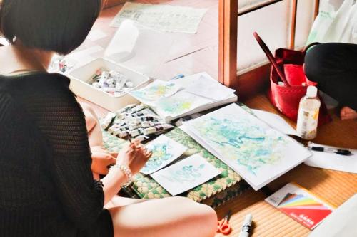 a woman sitting on a desk with art supplies at Guesthouse SETOUCHI LIFE in Kure