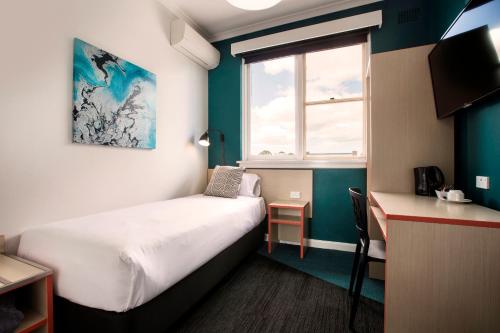 a bedroom with a bed and a desk and a window at Greenacre Hotel in Sydney