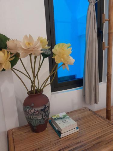 a vase with flowers on a table with a book at Tâm Homestay in Hue
