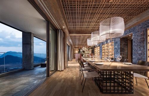 a dining room with a long table and chairs and windows at Tengchong Bodu Hot Spring Resort Hotel in Tengchong