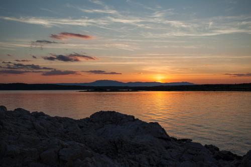 a sunset over a body of water with rocks at VSG Resort - Apartments 200m from Beach, Pool, Sauna & Jacuzzi in Klimno
