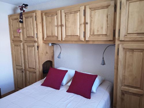 - un lit avec 2 oreillers rouges et des armoires en bois dans l'établissement Grand T2 résidence avec piscine sauna, à Huez