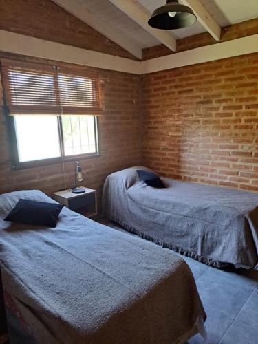 a bedroom with two beds and a brick wall at Los Chivos in Villa Cura Brochero