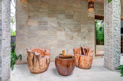a group of wood stools in front of a stone wall at Ganesh Lodge in Candidasa