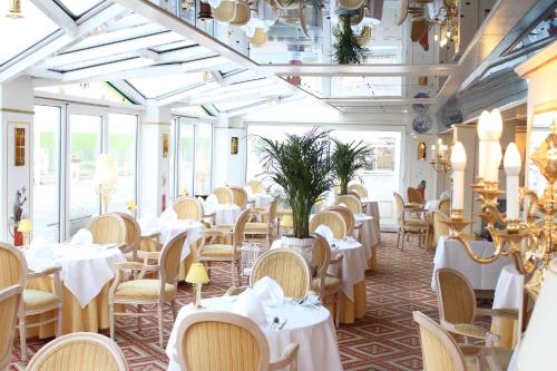 un restaurante con mesas y sillas blancas y ventanas en Seeschlößchen - Hotel Strandperle, en Cuxhaven