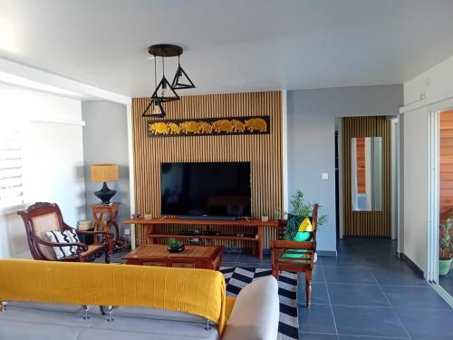 a living room with a yellow couch and a television at Villa Anj'any DESHAIES - 5 minutes à pieds de la plage in Deshaies