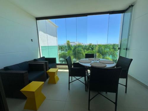a dining room with a table and chairs and a large window at Apartamento Iberostate Praia do Forte, 2 quartos in Mata de Sao Joao