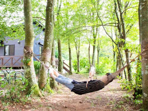 a man laying in a hammock in the woods at Starry Forest Inn KURIHAI in Oita