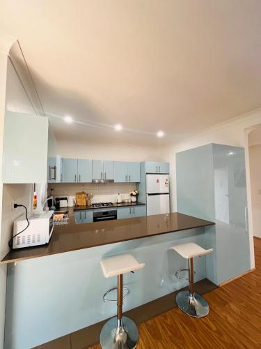 a kitchen with white cabinets and a counter with two stools at Lovely Modern Family home for your family and friends in Narwee