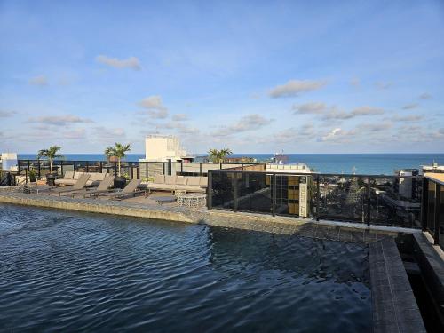 a pool of water with chairs and the ocean at Lindo Studio no Coração de Tambaú in João Pessoa