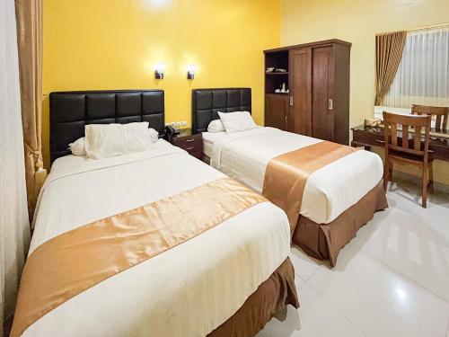 two beds in a hotel room with yellow walls at Kartika Hotel Syariah Pacitan Mitra RedDoorz in Pacitan