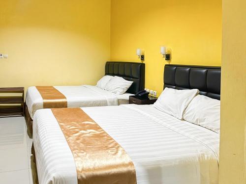 two beds in a hotel room with yellow walls at Kartika Hotel Syariah Pacitan Mitra RedDoorz in Pacitan