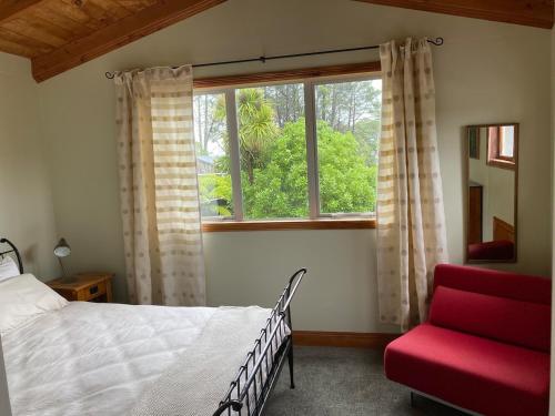 a bedroom with a bed and a window and a red chair at Above the Bay in Hahei