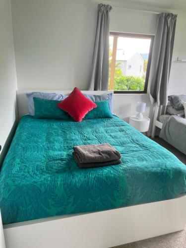 a bed with a green comforter and a red pillow at Spectacular Lake and Mountain Views Close to town in Queenstown