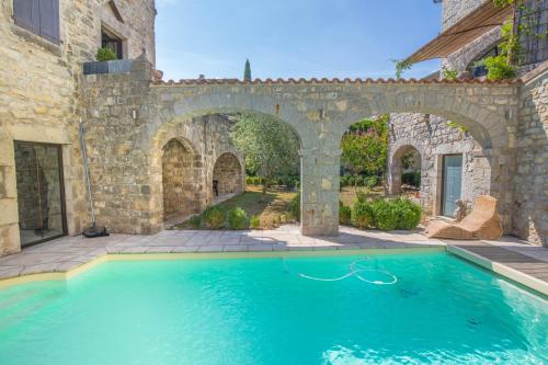 an outdoor swimming pool in front of a stone building with an arch at L Antre de Pierres - chambres d'hôtes et gites in Berrias Et Casteljau
