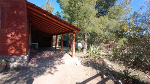 een overdekte veranda van een rood huis met bomen bij Al Pie Del Cerro Champaqui in Los Hornillos