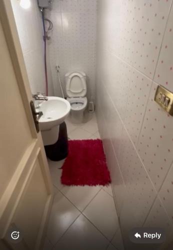 a bathroom with a toilet and a sink and a red rug at Panorama Elsherouk Furnished 2 bedroom apartment in Madīnat ash Shurūq