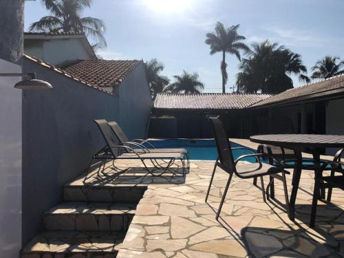 a patio with chairs and a table and a pool at Casa Maldonado Morada da Praia 4 suítes in Bertioga