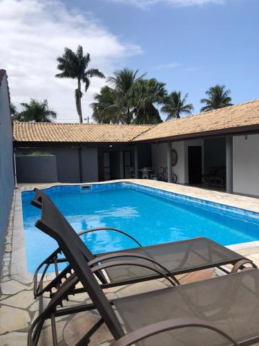 a blue swimming pool with a chair and palm trees at Casa Maldonado Morada da Praia 4 suítes in Bertioga
