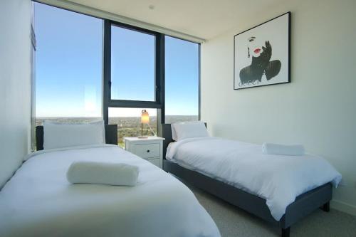 two beds in a room with a window at Serenity in the Sky - 2BR Apt in Rundle Mall in Adelaide