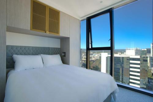 a bedroom with a white bed and a large window at Rundle Retreat - 2BR Apartment with stunning views in Adelaide