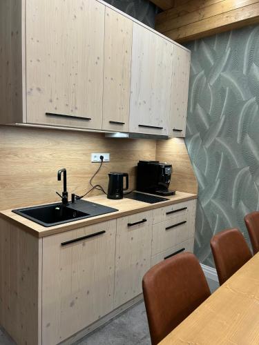 a kitchen with wooden cabinets and a sink and a table at Luxusní Apartmány Domovjanka - LYSÁ HORA, SMRK, KMÍNEK, SLAVÍČ in Bílá