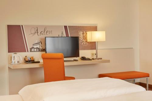 a room with a bed and a desk with a television at H+ Hotel Limes Thermen Aalen in Aalen