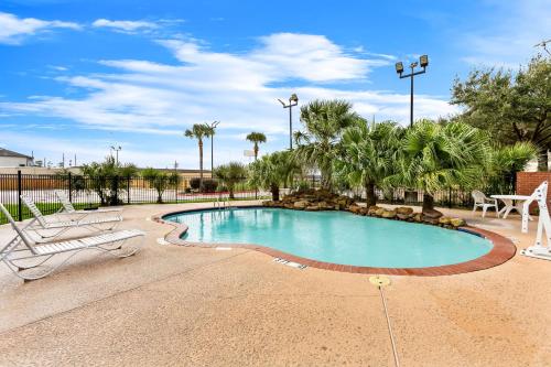 a swimming pool with two lounge chairs and palm trees at Sonesta Essential Beaumont in Beaumont