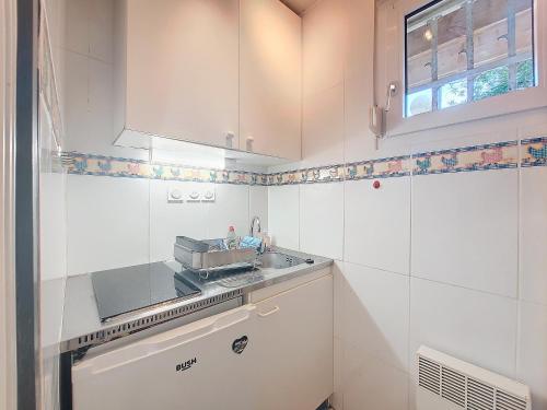 Elle comprend une petite cuisine blanche avec un évier et une fenêtre. dans l'établissement S-Plage 02-Soustons Joli petit appartement avec jardin et piscine pour 4 personnes, à Vieux-Boucau-les-Bains