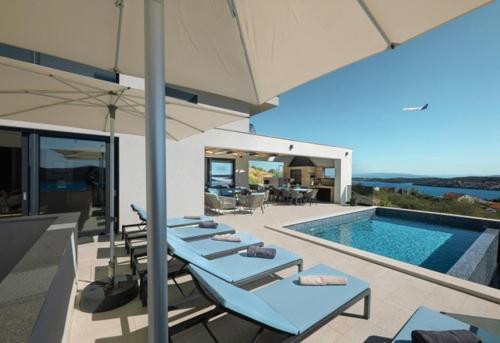 a group of lounge chairs with an umbrella next to a swimming pool at Villa Blue Horizon in Seget Vranjica