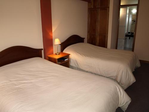 two beds in a hotel room with a lamp on a night stand at Qelqatani Hotel in Puno