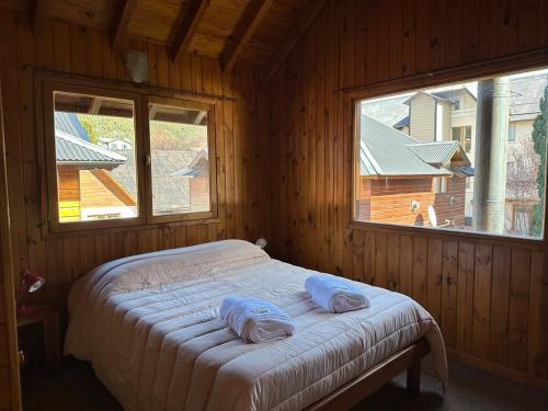 Cama en habitación de madera con 2 almohadas en Casita Roca - Pleno Centro, en San Martín de los Andes