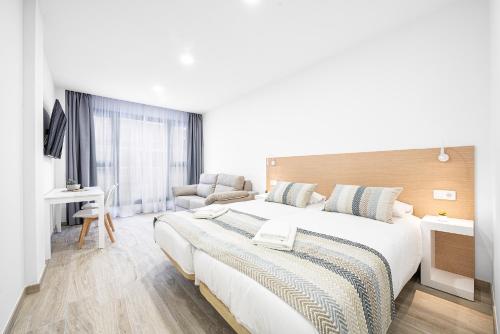 a white bedroom with a large bed and a chair at La Marquesa Ten Suites Canteras in Las Palmas de Gran Canaria