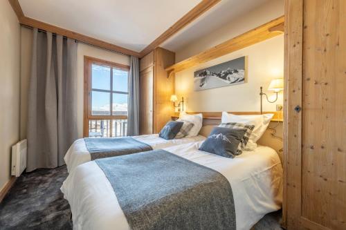 two beds in a hotel room with a window at Appt rénové, 6 personnes Arc 1950 vue exceptionnelle MontBlanc, sauna, hammam, piscine int et ext in Arc 1950