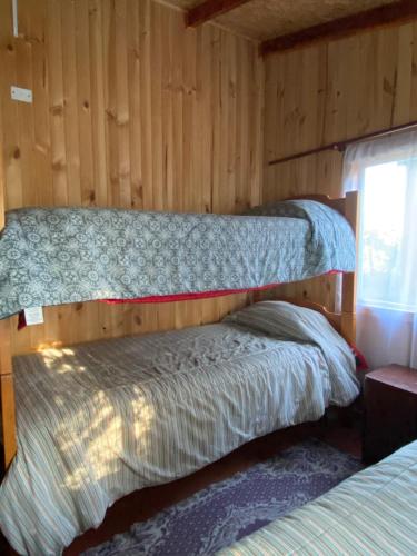 a bedroom with two beds in a wooden wall at Cabaña entre mares Huelmo in Puerto Montt