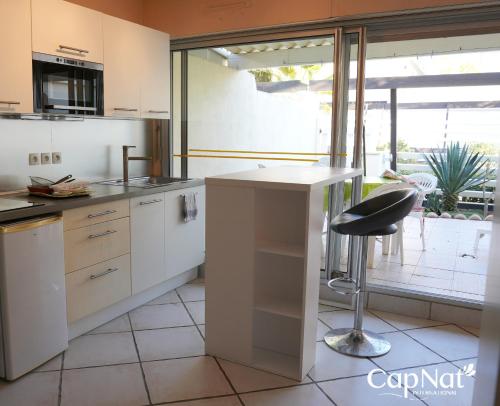 une cuisine avec des placards blancs et un tabouret noir dans l'établissement CapNat - Village Naturiste - Port Nature - Villa Dolce Vita, au Cap d'Agde