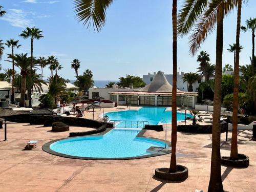 a swimming pool with palm trees in a resort at Villa Irene Lanzarote en Costa Teguise en complejo con piscina comunal in Costa Teguise