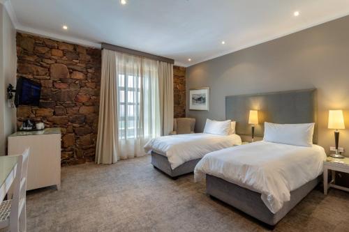 a bedroom with two beds and a stone wall at Protea Hotel by Marriott Mossel Bay in Mossel Bay