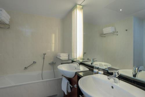 a bathroom with two sinks and a tub and a mirror at Sheraton Carlton Nuernberg in Nürnberg