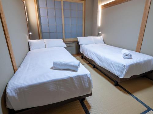 two beds in a small room with white sheets at Welcome Nozawa in Nozawa Onsen