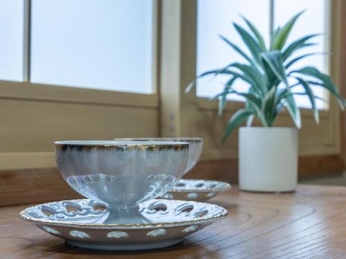 two bowls on a wooden table with a potted plant at Welcome Nozawa in Nozawa Onsen