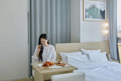 a woman talking on a phone next to a bed at Aank Hotel Sejong in Sejong