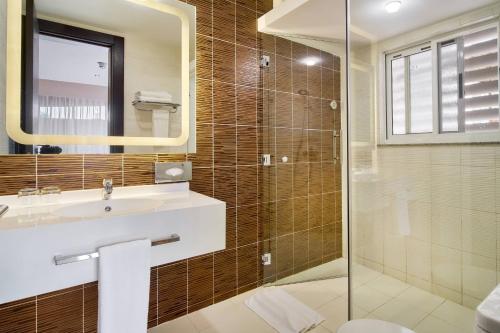 a bathroom with a sink and a glass shower at Protea Hotel by Marriott Kampala Skyz in Kampala
