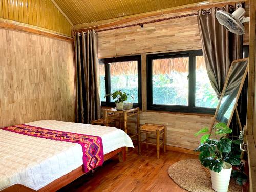 a bedroom with a bed and a table and windows at Maison De Mai Hich in Mai Châu
