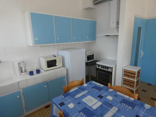 une cuisine avec des placards bleus, une table et un four micro-ondes dans l'établissement Appartement 39m², 1 chambre, animaux admis, parking, forêt, 5 pers - Notre-Dame-de-Monts - FR-1-540-297, à Notre-Dame-de-Monts
