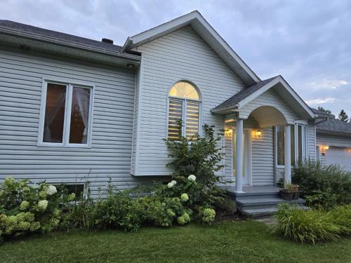a gray house with a porch and flowers in the yard at Villa Des Petits Bonheurs in Lac-Simon