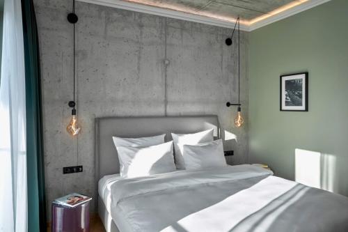 a bedroom with a white bed with a concrete wall at Gekko House Frankfurt, a Tribute Portfolio Hotel in Frankfurt/Main