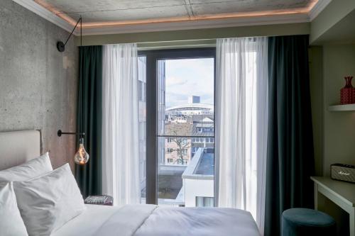 a bedroom with a bed and a large window at Gekko House Frankfurt, a Tribute Portfolio Hotel in Frankfurt/Main