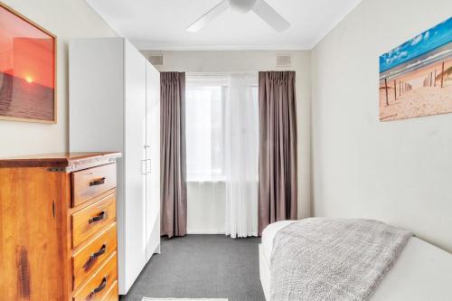 a bedroom with a bed and a dresser and a window at Semaphore's Seaside Retreat in Semaphore