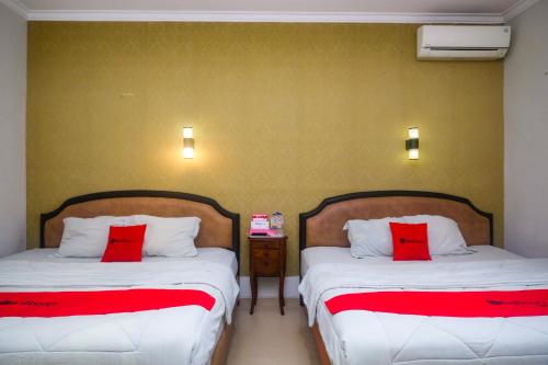 two beds in a room with red pillows at RedDoorz Plus near Adisucipto Airport 2 in Yogyakarta